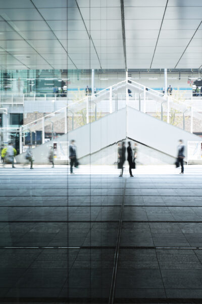 people walking by a glass building, you can see their reflections in the glass