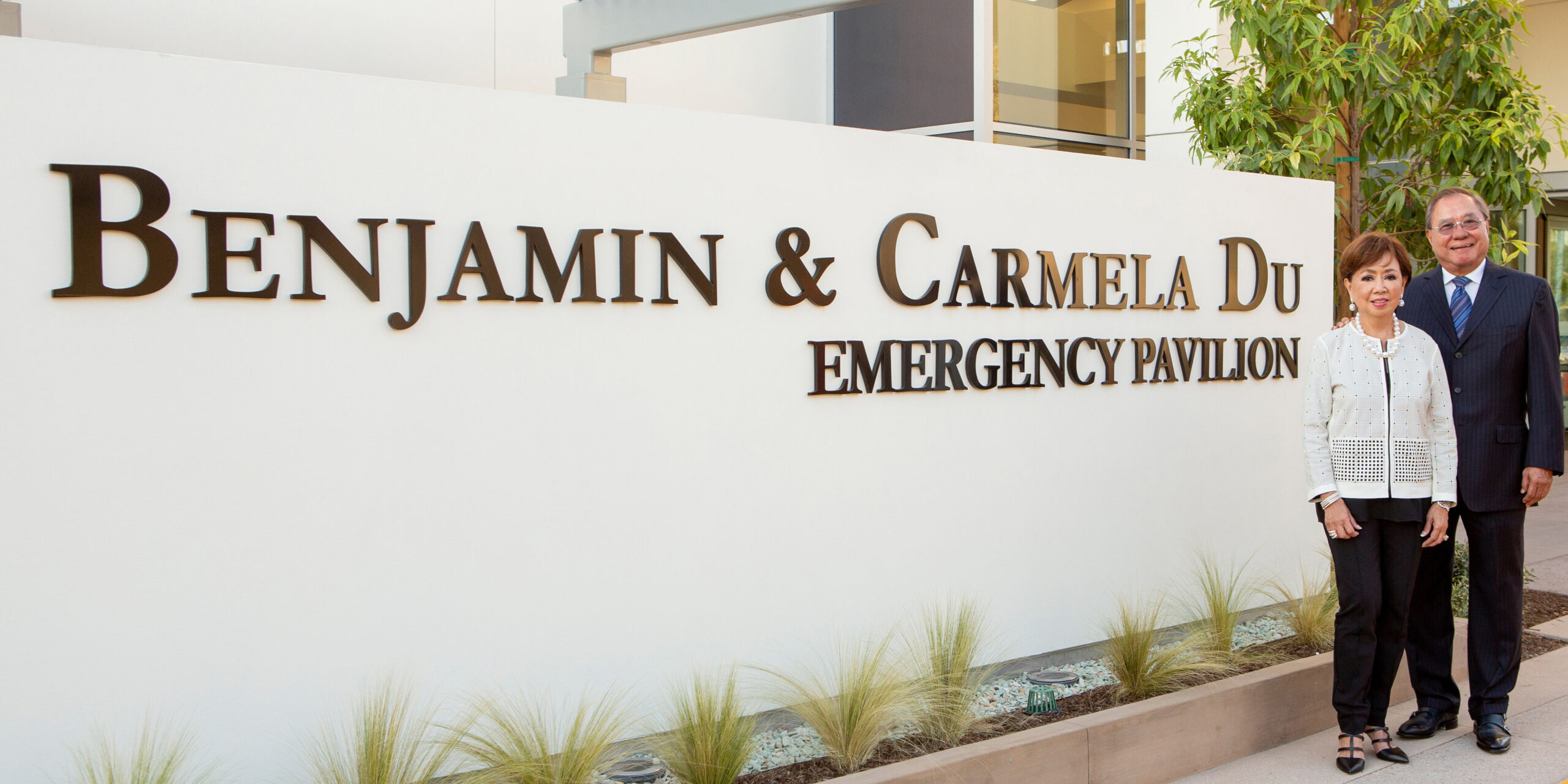 2024 Carmel and Ben Du Approved photo3 Carmela and Benjamin Du standing next to a sign for the Benjamin & Carmela Du Emergency Pavilion