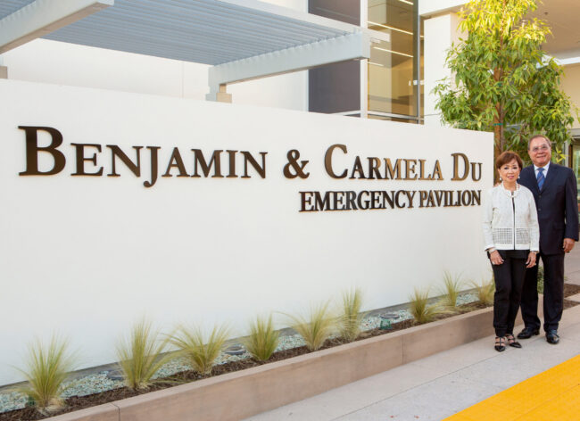 2024 Carmel and Ben Du Approved photo3 Carmela and Benjamin Du standing next to a sign for the Benjamin & Carmela Du Emergency Pavilion